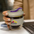 A drink bottle with a grey and purple design, featuring a logo, held in a hand near a laptop.