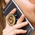 A bamboo phone holder in a woman's hand, securely attached to a grey smartphone, featuring a logo on the holder.