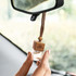 A refillable car air freshener with a wooden cap and clear glass container, hanging from a car mirror.