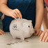 A piggy bank in a natural speckled finish, with a small logo on the side, surrounded by coins on a table.