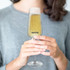 A clear champagne flute filled with bubbly, held by a person wearing a grey sweater. The glass has a logo.