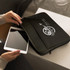 A small black laptop sleeve with a logo, being opened to reveal a tablet inside.