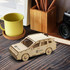A wooden SUV model in natural wood finish with a logo, placed on a wooden surface near a cup and camera.