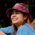 A red and black check-patterned bucket hat with a logo, worn by a smiling individual outdoors.