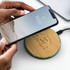 A bamboo wireless charger with a black base and a smartphone being placed on it, featuring a logo.