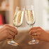 Two elegant glass champagne flutes filled with bubbly champagne, clinking together. Both glasses have a logo.