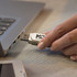 A white 8GB flash drive is being plugged into a laptop. The device features a logo on its surface.