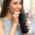 A black vacuum tumbler with a straw, featuring a logo, held by a person outdoors.