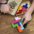 A colourful wooden pentomino puzzle set displayed on a wooden surface, with hands assembling the pieces.