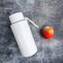 A drink bottle in sleek white stainless steel with a removable straw, accompanied by a red apple.