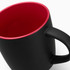 A coffee mug with a matte black exterior and a red interior, featuring a handle and a logo.