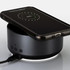 A black wireless charging speaker with a smartphone placed on top, displaying a charge indicator.
