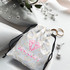 A small white satin gift bag with a drawstring, featuring a pattern and a logo, alongside rings and pearls.