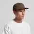 A cap in a muted brown colour worn by a model, featuring a simple design and a logo.