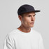 A black cap with a flat peak, featuring mesh panels for breathability. The model is wearing a white T-shirt.