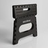 A black folding stool with a textured surface and a handle, featuring a logo on the front.