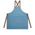 A denim apron in blue with brown straps and a front pocket, featuring a logo.