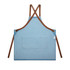 A denim apron in light blue with brown straps and a front pocket, featuring a small logo.