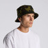 A camo bucket hat in green and black, featuring a wide brim and a logo on the side.