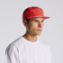 A red cap with a flat brim, featuring a logo and worn by a model against a neutral background.