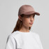 A pink cap with a curved brim, featuring a logo on the front and worn by a model with long hair.