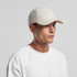 A beige nylon cap with a curved brim, worn by a model in a white t-shirt, featuring a logo on the front.