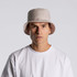 A light beige bucket hat with a wide brim, featuring a simple design and a logo.