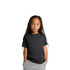 A black kids' heavy faded tee with short sleeves, worn by a child with long hair, standing with hands in pockets.