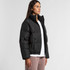 A black puffer jacket with a high collar and side pockets, worn by a model standing against a neutral background.