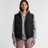 A black puffer vest worn over a grey hoodie, featuring a zip front and a logo. Model stands against a plain background.