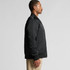 A black college bomber jacket displayed on a model in profile view, featuring a logo on the chest and ribbed cuffs.