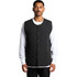 A black quilted vest with snap buttons, worn over a white long-sleeve top. The vest has a quilted texture and a minimal design.