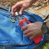 A drink bottle with a red silicone sleeve and a metal cap is being placed into a blue backpack.