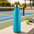 A drink bottle in vibrant blue with a stainless steel lid, placed on a surface near a tennis court.