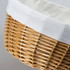 A wicker tote bag in natural bamboo tones with a cream-coloured fabric lining at the top and a textured weave pattern.