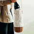 A drink bottle is nestled in a cream canvas and wicker wine carrier, held by a person. The carrier has a logo.