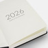 A 2026 daily planner with a cream interior and black exterior, featuring a minimalistic design and a logo.