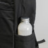 A black backpack pocket holds a silver-capped drink bottle, featuring a textured fabric design.