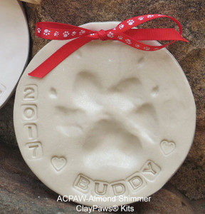 Almond Shimmer ClayPaws® pet paw print impression made from almond-colored modeling compound with a subtle shimmer finish, paw impression, stamped lettering, and ribbon.

