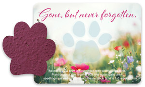 Purple paw-shaped seed paper displayed beside a floral memorial card with a translucent paw print and the phrase “Gone, but never forgotten.”

