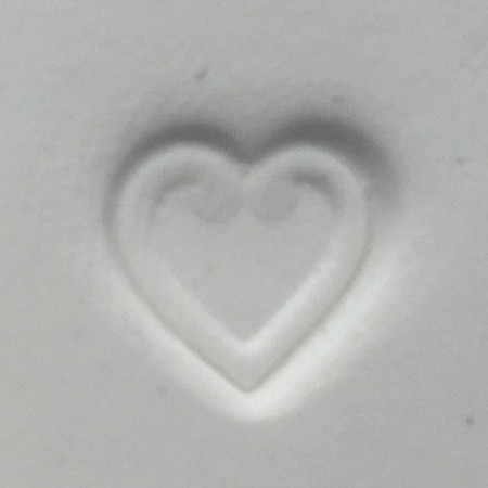 Heart-shaped impression pressed into white clay using the Pawprint Impression Kit Heart Stamp accessory with a detailed heart outline design.

