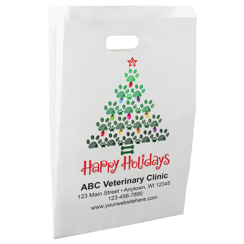 White die-cut handle paper bag featuring a Christmas tree made of green paw prints, colorful holiday lights, a red paw print star, and the message "Happy Holidays".

