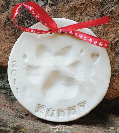 Original White ClayPaws® pet paw print impression keepsake made from white modeling compound with a paw print impression, stamped lettering, date markings, and red paw-print ribbon.

