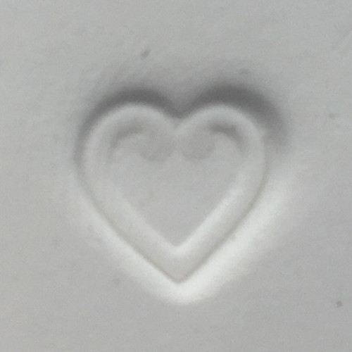 Heart-shaped impression pressed into white clay using the Pawprint Impression Kit Heart Stamp accessory with a detailed heart outline design.

