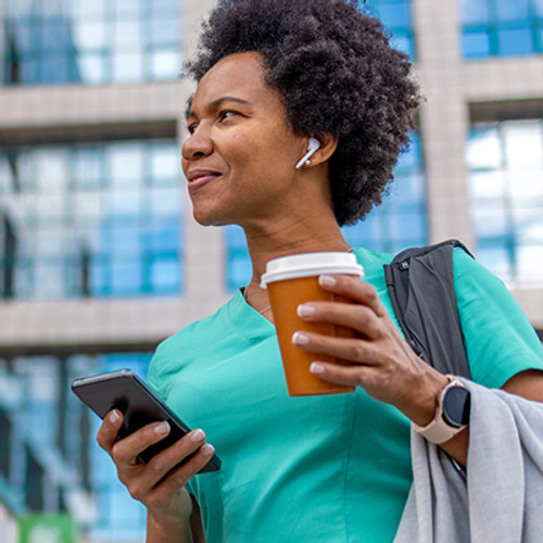 female doctor holding a cell phone and coffee while walking outside