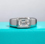 emerald-cut moissanite men’s ring displayed on turquoise background showing rhodium finish and sleek modern bezel setting