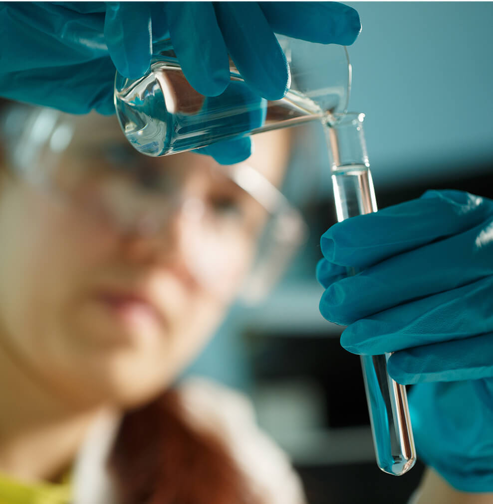 A woman wearing eye protection transfers liquid into a vial.