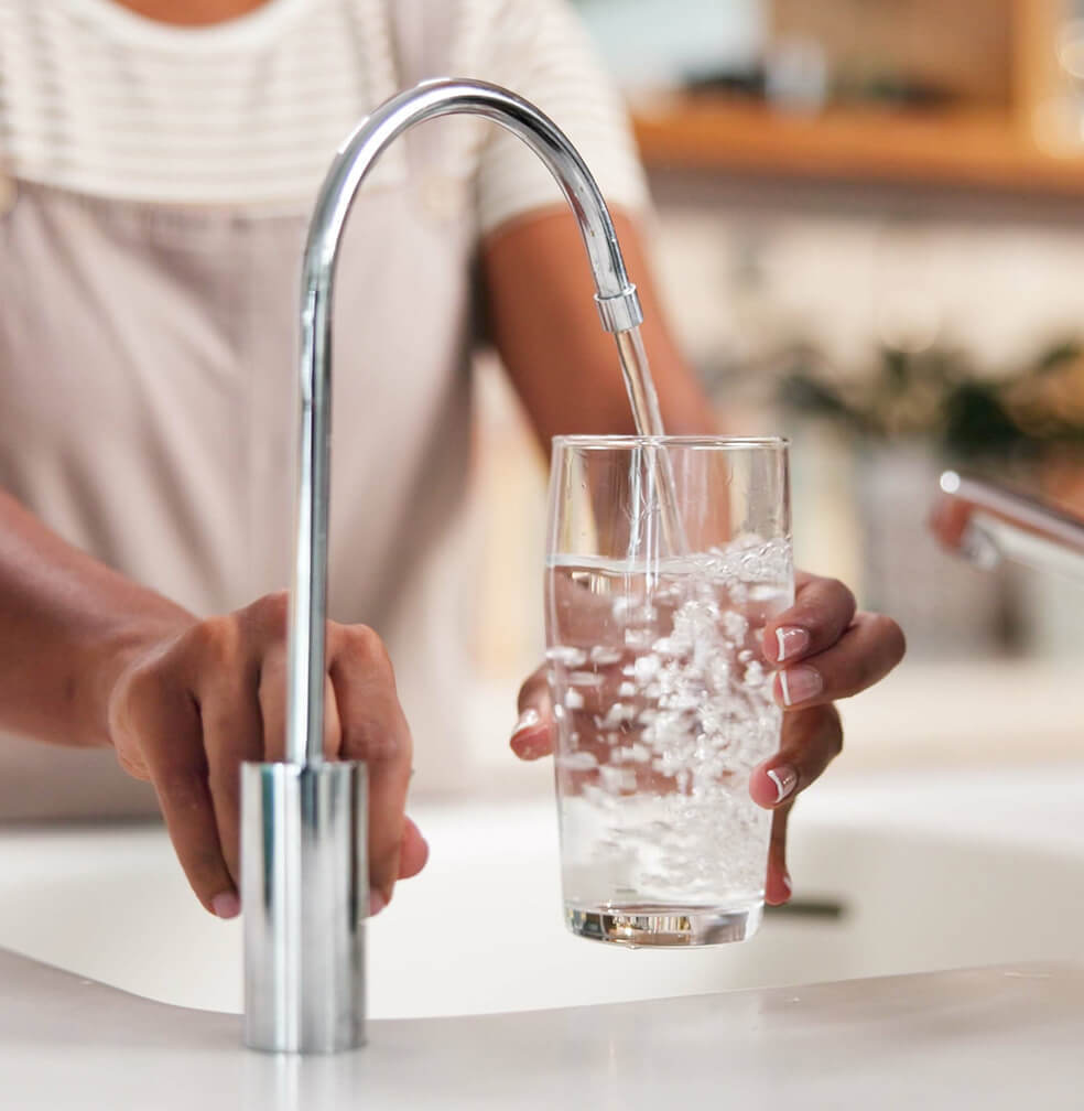 Close up of a woman filling a glass with filtered water from a kitchen sink.