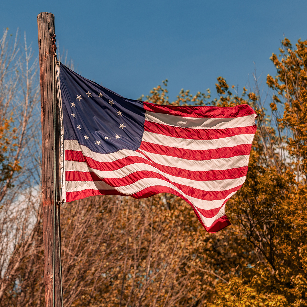 The "Betsy Ross" flag with a circle of 13 white stars waves on a wooden pole