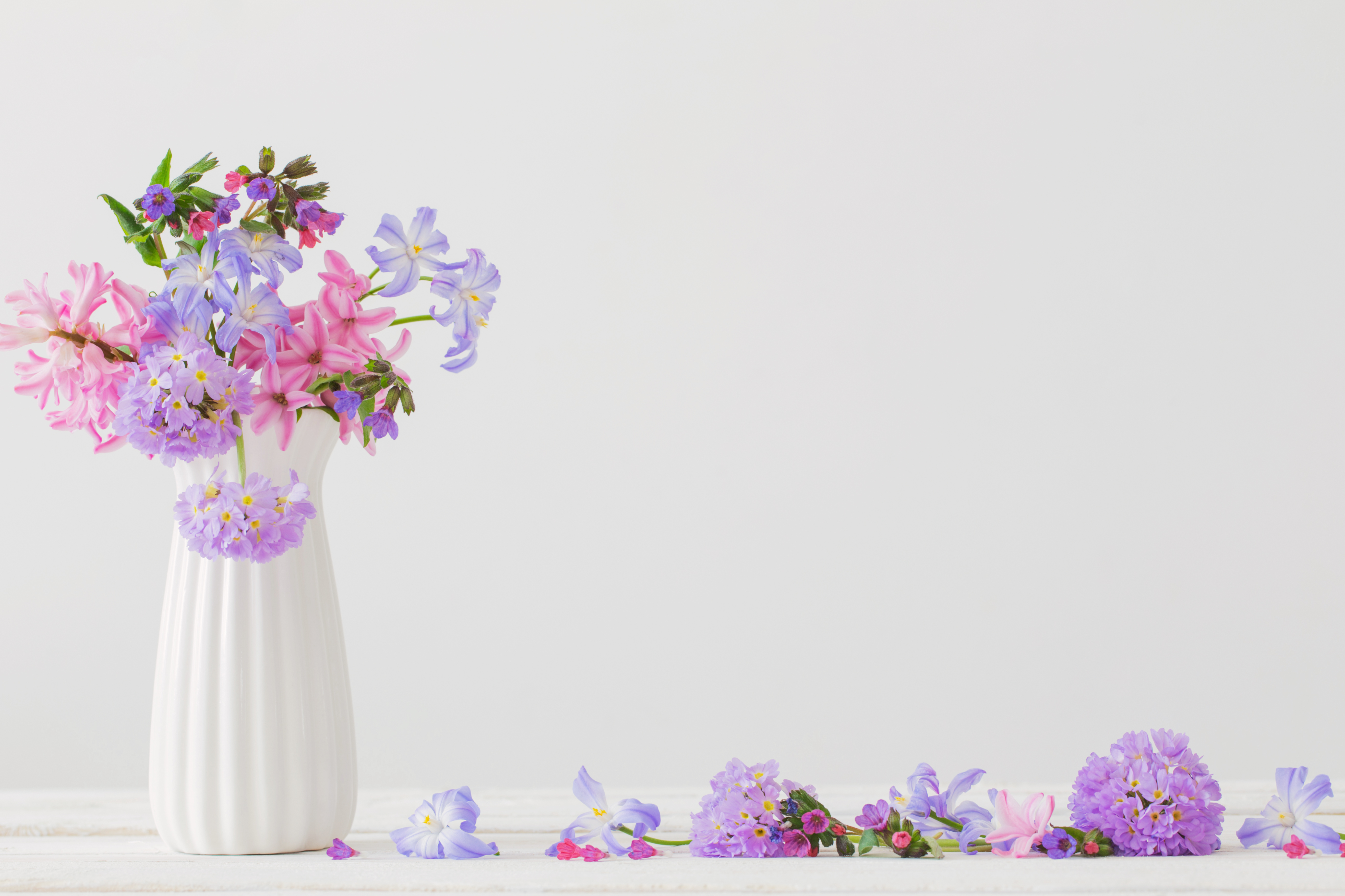 white vase filled with pink and lavender flowers with scattered petals on table